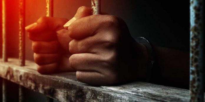 Close up prisoner holding bar in jail. Fotosearch